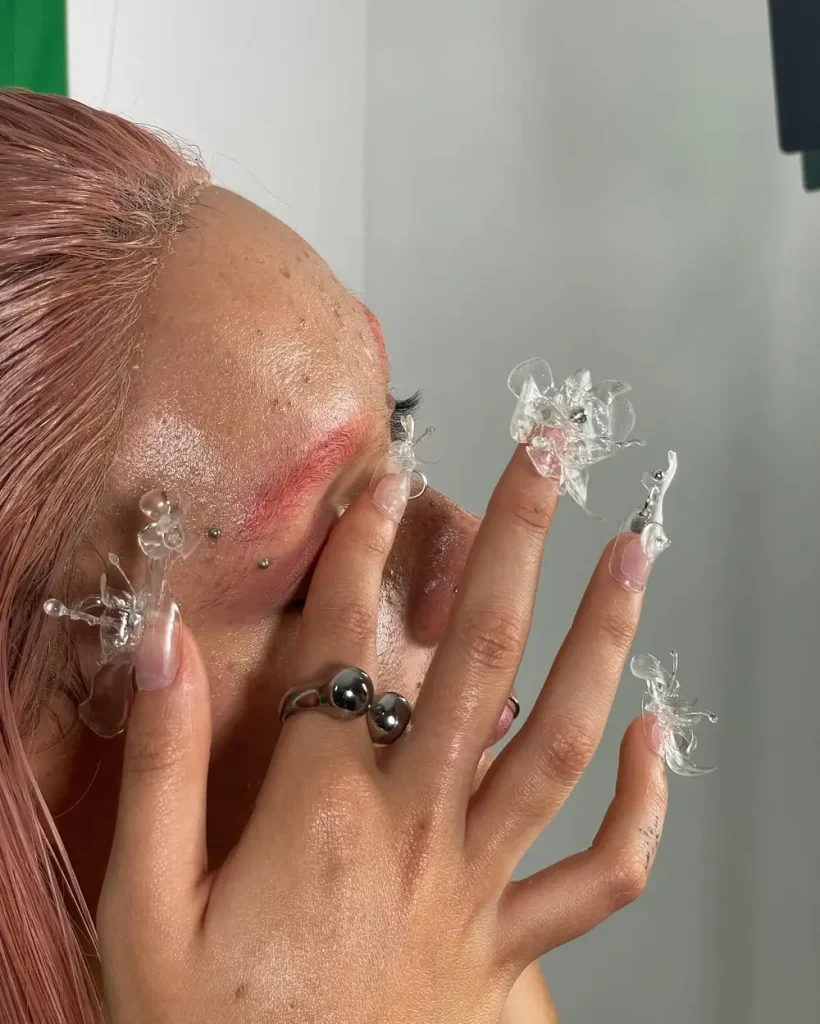 Primer plano de un rostro con maquillaje artístico y accesorios de cristal en los dedos.